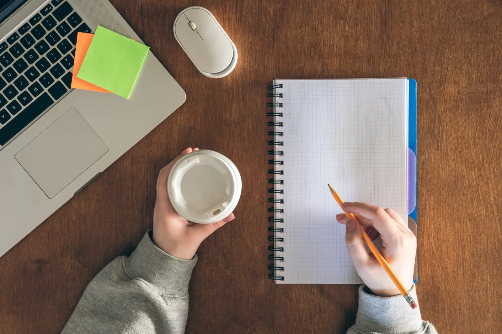 A notepad being written in beside a laptop, coffee and sticky notes, seen from above.