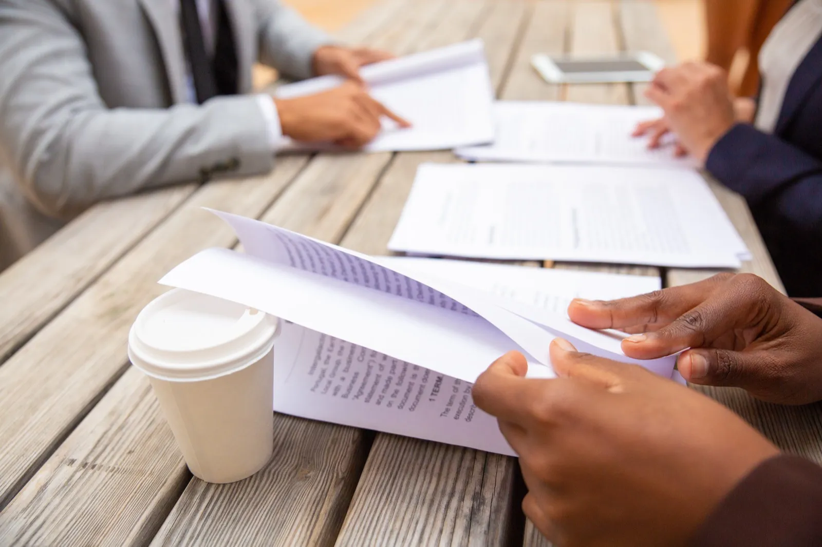 Hands passing printed pages across a table with coffee cups on it.