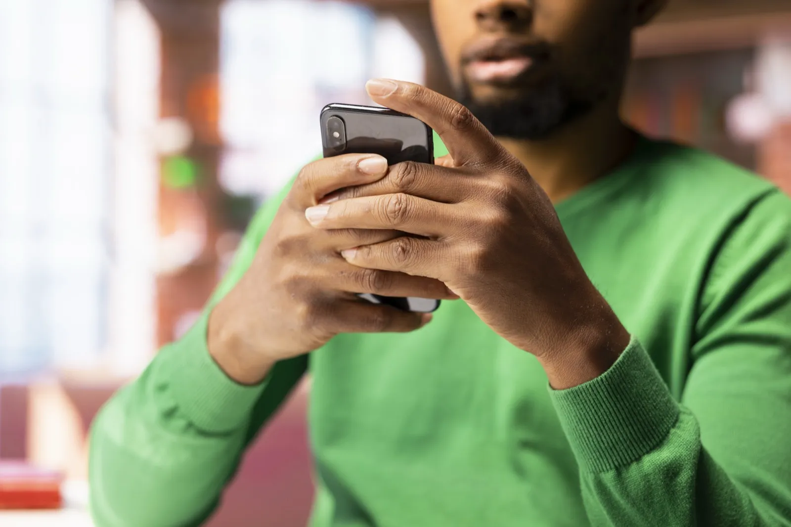 A man reads his phone, both thumbs on the screen.