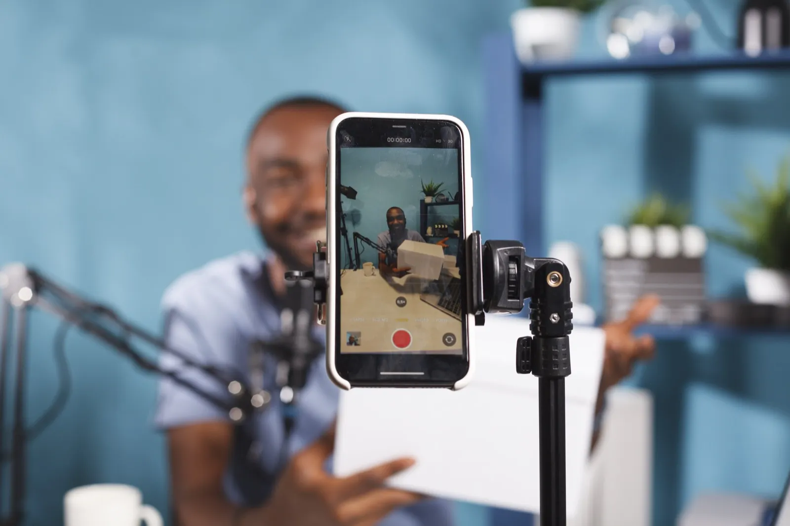 A phone on a rig recording a man holding a parcel, his face on its screen.