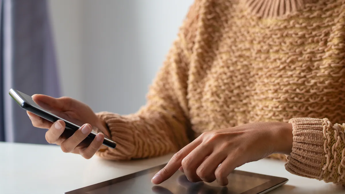 Hands at a white desk working a phone and a tablet together.