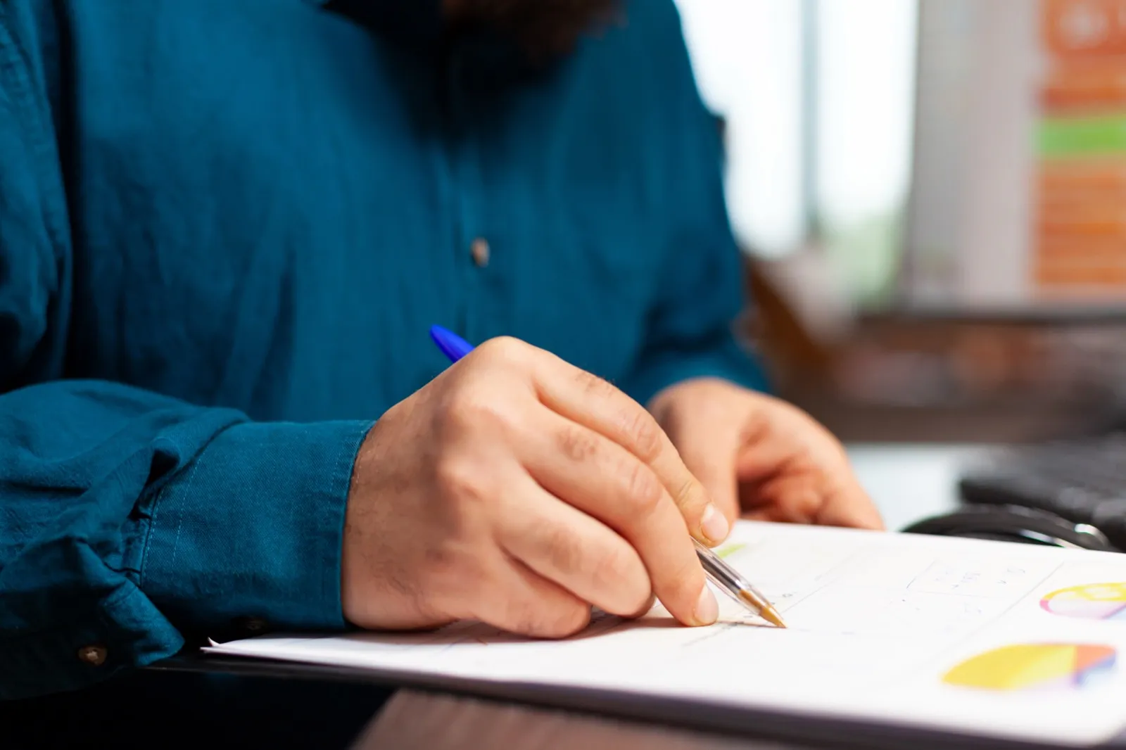 A hand holds a pen over a printed page of charts, tracing a line.