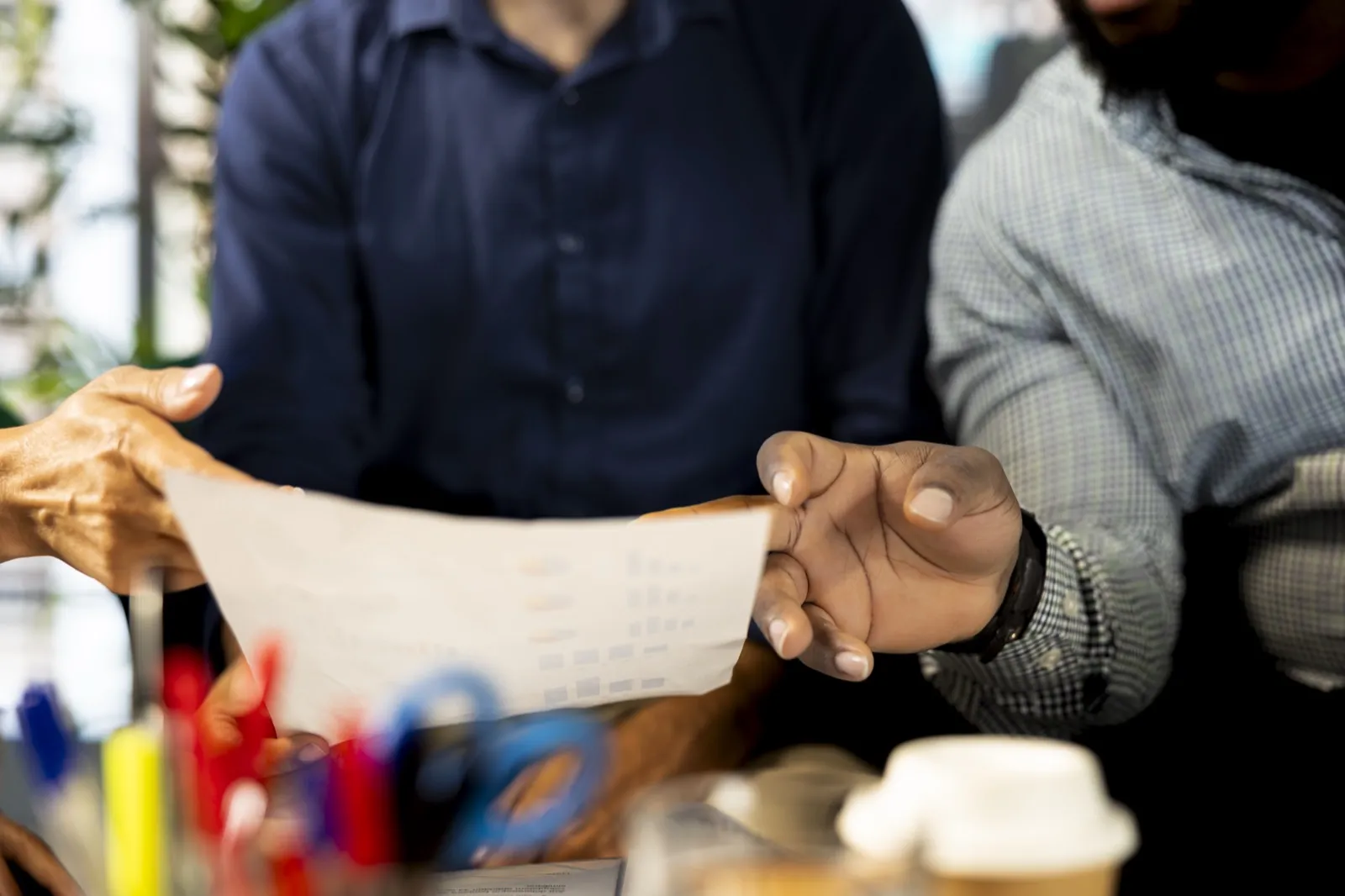 Two people passing a printed page of figures across a desk.