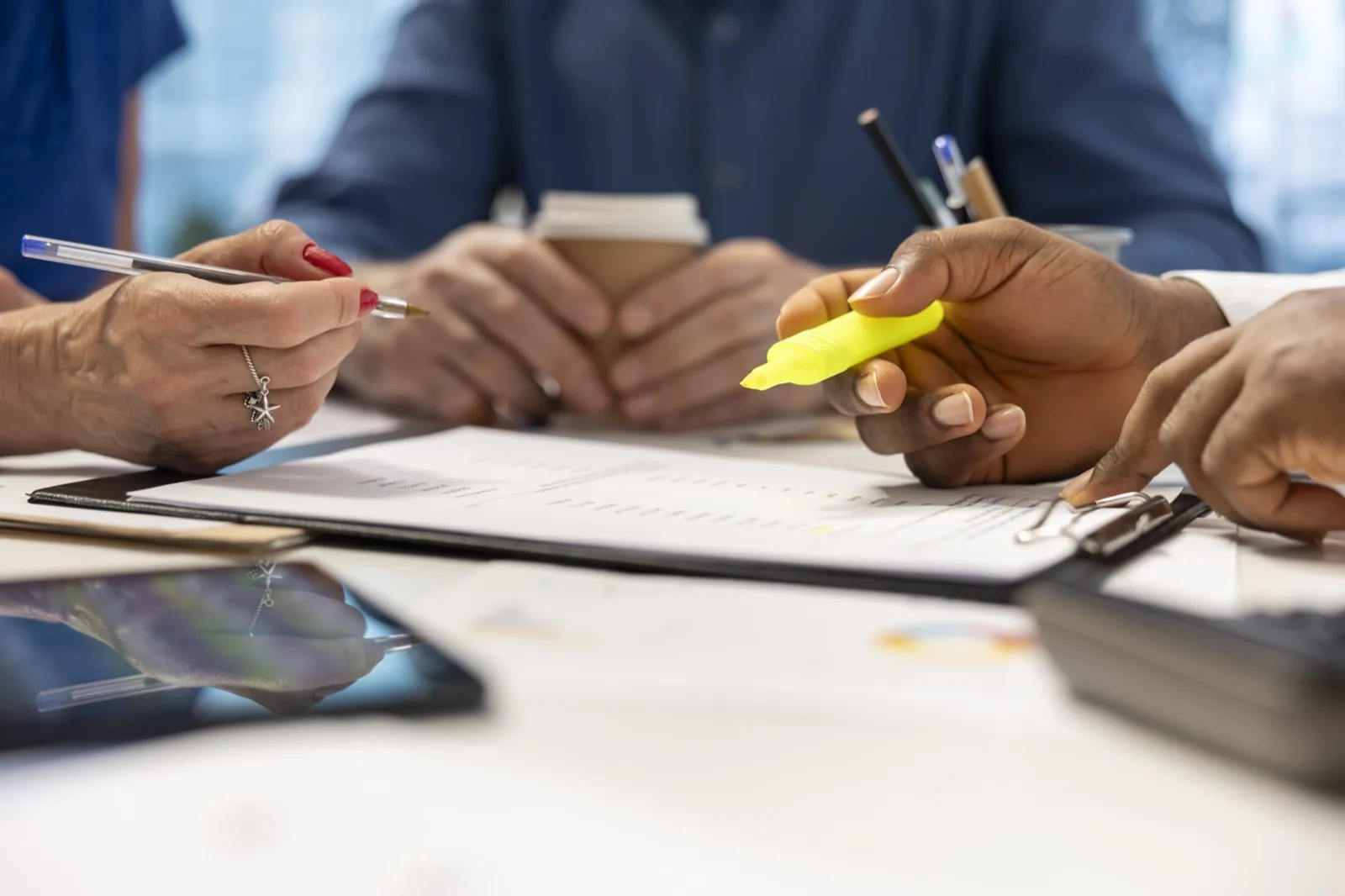 A hand runs a highlighter across a document at a table of people.