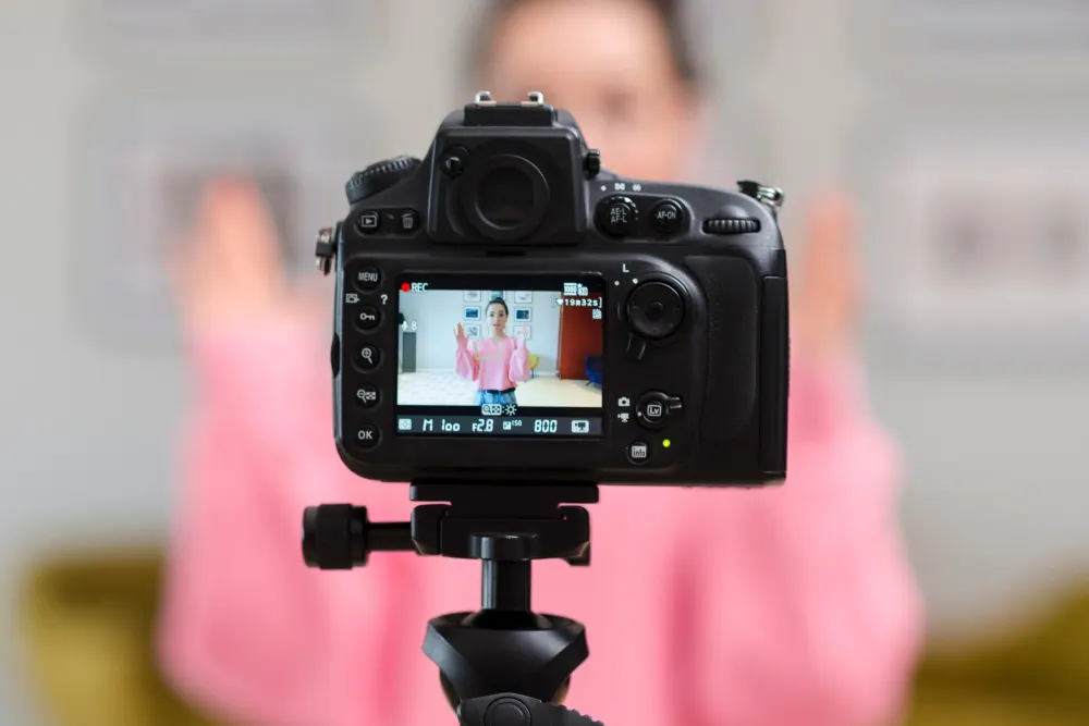 A camera on a tripod, its screen showing the person it is recording.