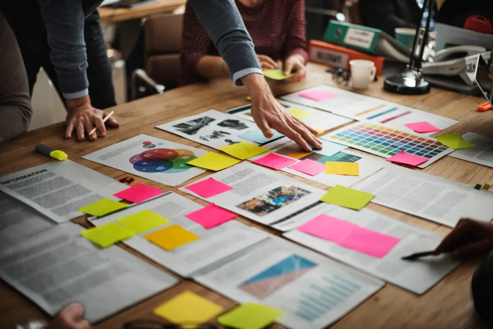 Two people leaning over a table of printed articles, colour swatches and sticky notes.